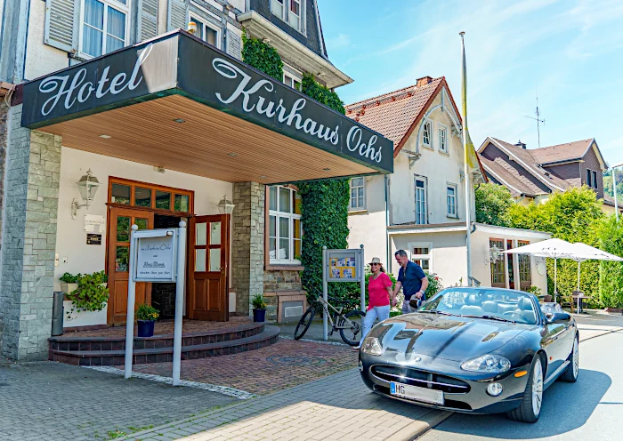 Ein Auto hält vor dem Hotel Kurhaus Ochs und 2 Gäste gehen zum Hoteleingang.